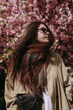 Portrait of beautyful woman with shaking long brown hair in sunglasses on the blossomed flowers background