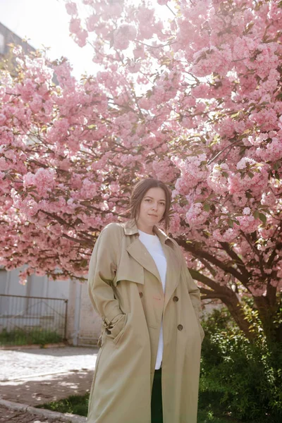 Arka planda çiçek açan palto giymiş şık Asyalı bir kadın.