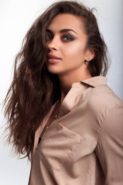 Stüdyo profilinde beyaz arka planda duran uzun kahverengi saçlı güzel Hintli kadın kameraya azgın bakışlarla bakıyor. 