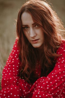 Kırmızı elbiseli güzel bir kadın çayırda poz veriyor.