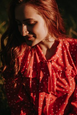 Siyah elbiseli, kızıl saçlı güzel genç bir kadın aşağıya bakıyor.