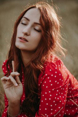 Kırmızı elbiseli, güzel, genç bir kadın. Kapalı gözlerle çayırda oturuyor ve bir şeyin hayalini kuruyor.
