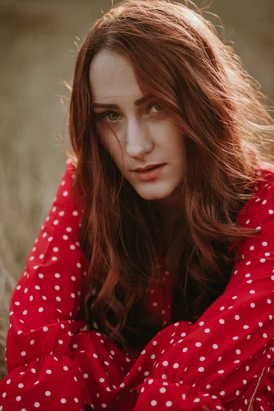 Kırmızı elbiseli güzel bir kadın çayırda poz veriyor.