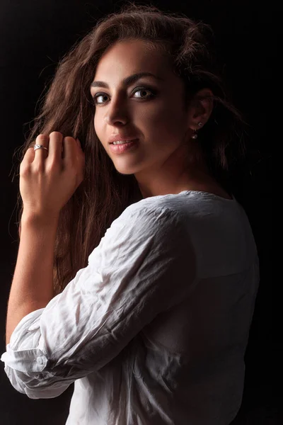 Siyah arka planda beyaz pamuklu gömlekli, uzun saçlı güzel bir kadın.