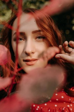 Kızıl saçlı kadın, ormanın arka planındaki kuru çim tarlasında kamera önünde poz veriyor.