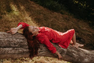 Kırmızılı, beyaz benekli, genç ve güzel bir kadın ormanın ortasındaki kurumuş bir ağaç gövdesinde uyuyor.