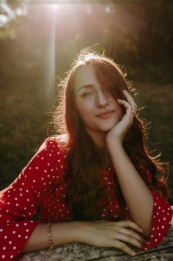 Kapalı yüz portresi güzel beyaz beyaz kadın kırmızı uzun kıvırcık saçlı, kırmızı gömlekli, başını tutuyor ve kameraya bakıyor.