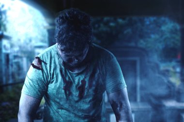 Mezarlıkta yürürken vücudunda kan ve yara olan korkunç bir zombi.