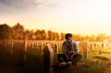 Mezarlıkta oturan, üzerinde kan ve yara olan korkunç bir zombi.