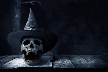 Ahşap masanın üzerinde insan kafatası, koyu renkli bir şapka.