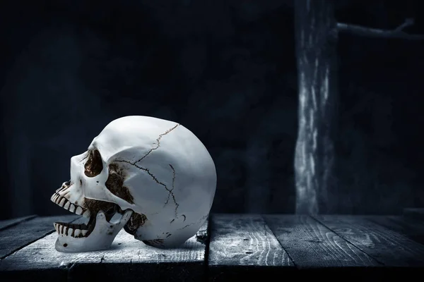 暗い背景を持つ木製のテーブルの上に人間の頭蓋骨 — ストック写真
