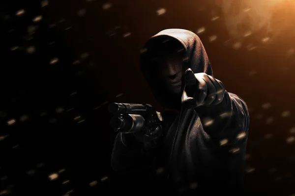 A criminal man in a hidden mask hold the shotgun and points something with dramatic background