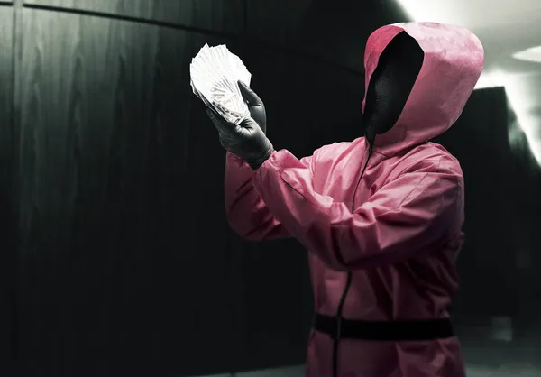 Criminal man in pink uniform and a hidden mask holding the money after the robbery the house