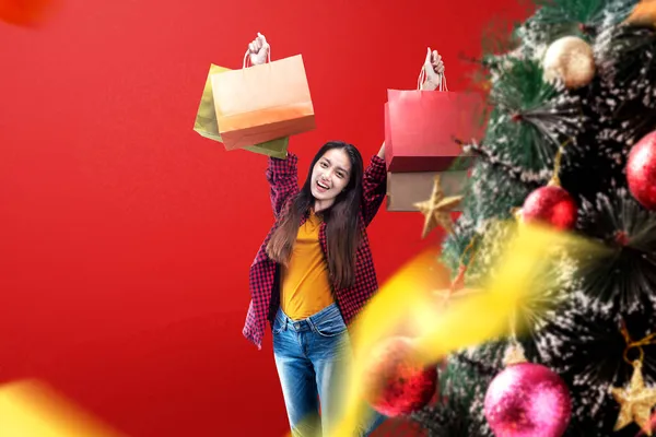 Geschmückter Weihnachtsbaum Mit Asiatischer Frau Die Einkaufstüten Auf Farbigem Hintergrund — Stockfoto