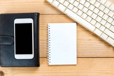 Computer keyboard and note book with a mobile phone on wooden desk