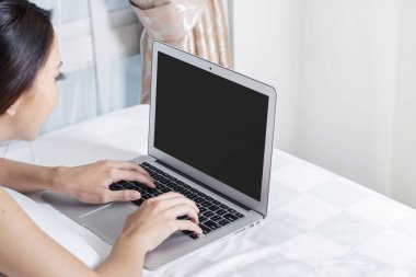 Yatakta dizüstü bilgisayar kullanarak uzanan Asyalı kadın.