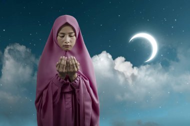 Duvak takmış Asyalı Müslüman kadın el kaldırdı ve gece sahne geçmişi ile dua etti.