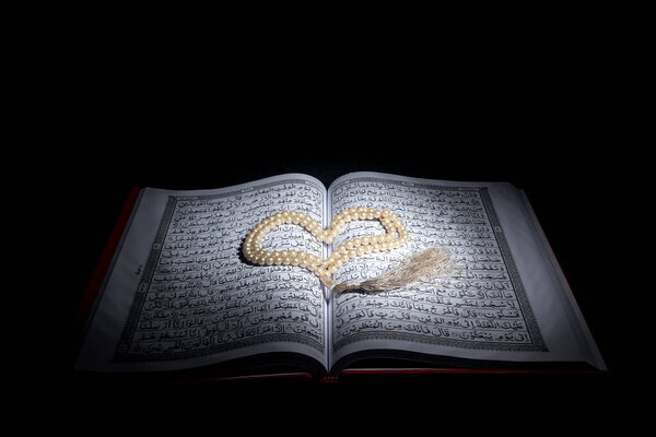 Quran open with prayer beads with dark background