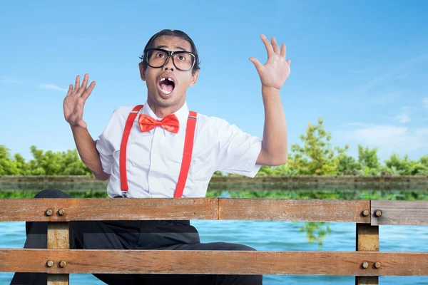 Asian nerd with ugly face falling from wooden fence to the lake