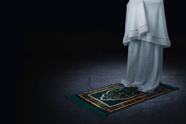 Namaz kılarken, arka planı koyu renk olan müslüman bir kadın.