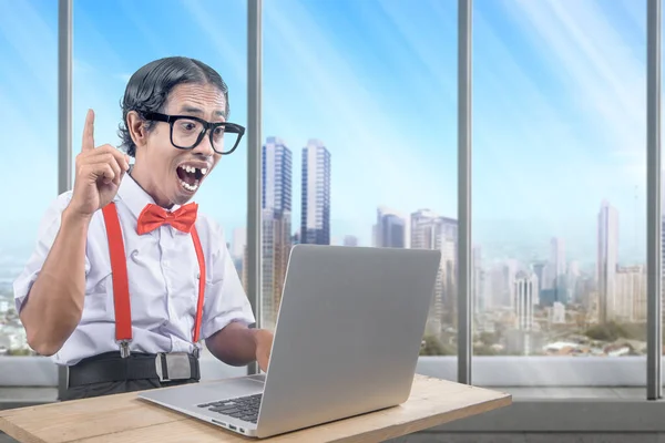 Asian nerd with an ugly face using laptop inside the room with a window glass background