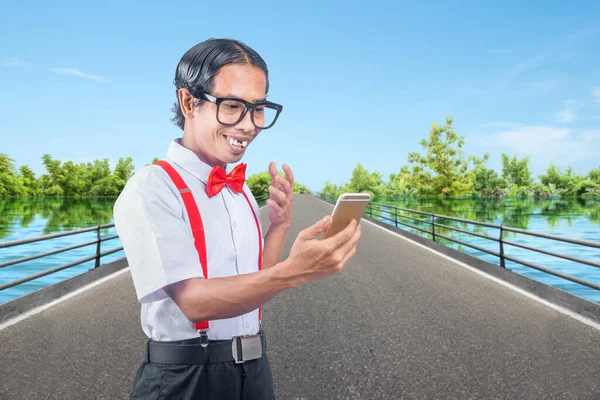 Asian nerd with an ugly face holding mobile phone on the street