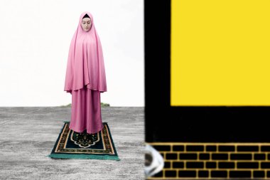 Mavi arka planda Kabe 'nin önünde namaz kılan Asyalı Müslüman kadın.