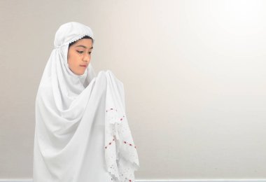 Duvak takmış Asyalı Müslüman kadın elini kaldırdı ve beyaz arka planda dua etti.