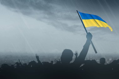 Ukrayna bayrağını yağmurlu arka planda tutan kalabalığın silueti