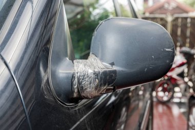 Siyah arabanın yan aynası kırılmış ve garajdaki bantla yapıştırılmış.