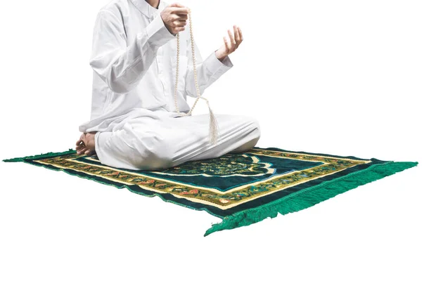 白い背景に隔離された祈りの敷物の上に座っている間 彼の手に祈りのビーズで祈るイスラム教徒の男 — ストック写真