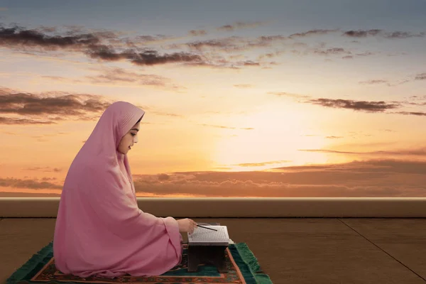 ベールを着たアジア系ムスリム女性がクルアーンを朗読し 劇的な場面を背景にしています — ストック写真