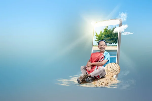 有海滩景观的手机屏风 电话里传来一个亚洲男人 他坐在海滩上抱着他的背包 戴着一顶便帽 旅行概念 — 图库照片