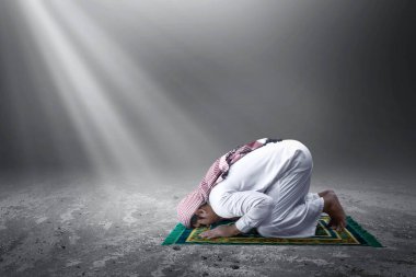 Kefiyeh 'li Müslüman bir adam, namaz kılma pozisyonunda, arka planda hafif bir duayla.