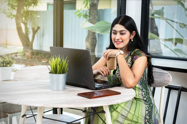 Indian woman with laptop on the table holding coffee in the coffee shop