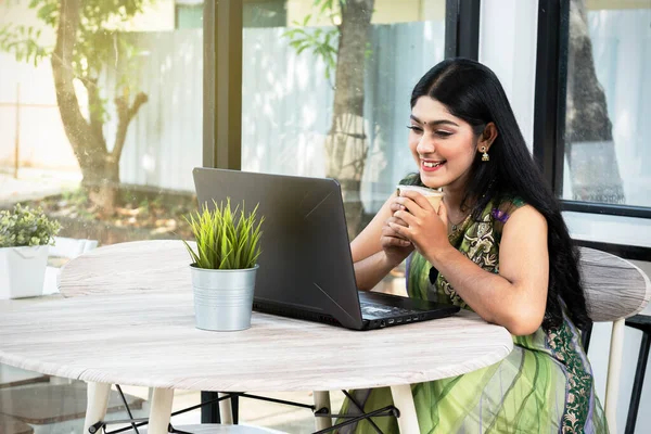 Indian woman with laptop on the table holding coffee in the coffee shop