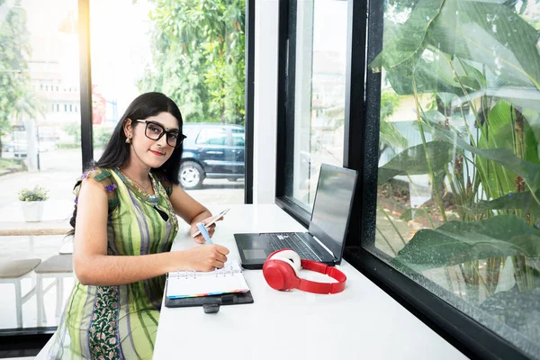 Indian Woman Eyeglasses Writing Something Notebook While Holding Mobile Phone —  Fotos de Stock