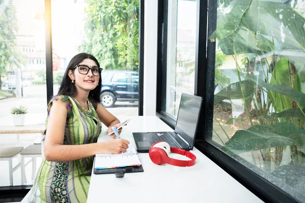 Indian Woman Eyeglasses Writing Something Notebook While Holding Mobile Phone —  Fotos de Stock