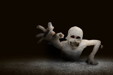 Mummy with skull head crawling with a dark background. Halloween concept