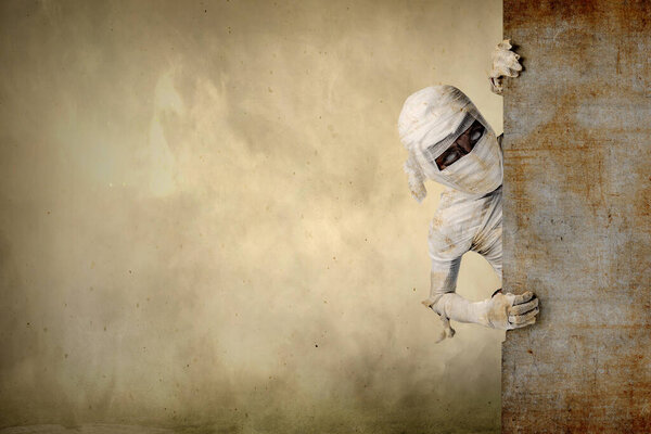 Mummy comes from behind the wall with a foggy background. Halloween concept
