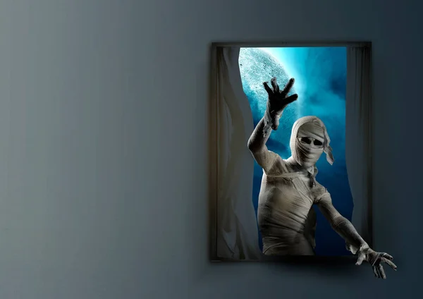 Mummy with a skull head and claw hands standing on the window with a night scene background. Halloween concept