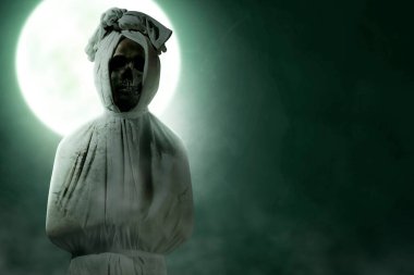Pocong is covered with a white linen shroud standing with full moon background. Halloween concept