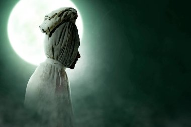 Pocong is covered with a white linen shroud standing with full moon background. Halloween concept