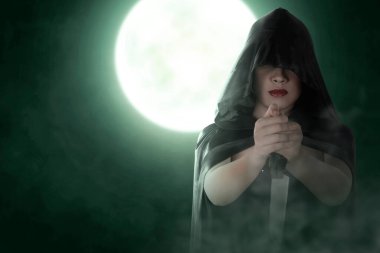 Asian witch woman with a cloak holding a knife standing with full moon background
