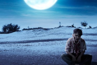 Vücudunda kan ve yara olan korkunç bir zombi. Sahada oturuyor.