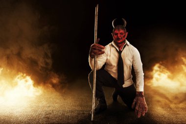 Devilman sitting while holding sticks with fire's background. Halloween concept