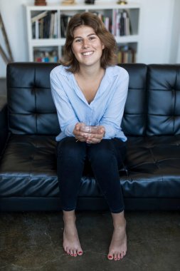 kanepede oturan ve su tutan çekici gülümseyen genç kadın