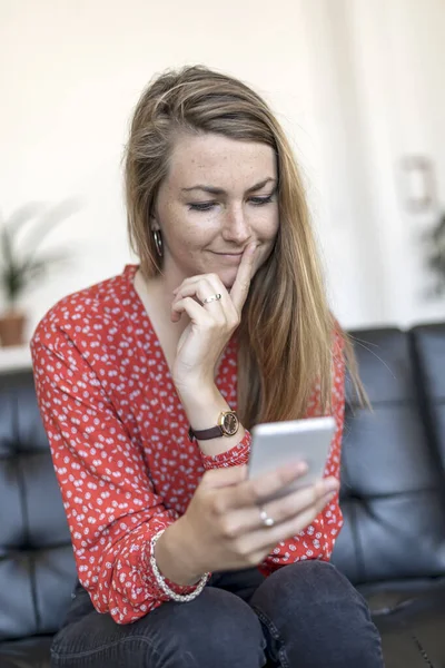 Mujer Sonriente Casa Sentada Sofá Mirando Teléfono Celular — Foto de Stock