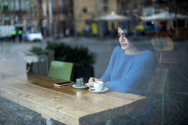 Genç model uzun siyah saçlı kadın brunch sırasında bir kahve dükkanında oturuyor. Latin kadın kafede masada otururken aşağı bakıyor..