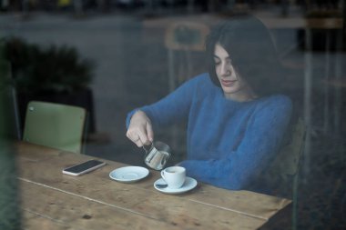Genç model uzun siyah saçlı kadın brunch sırasında bir kahve dükkanında oturuyor. Latin kadın kafede masada otururken aşağı bakıyor..